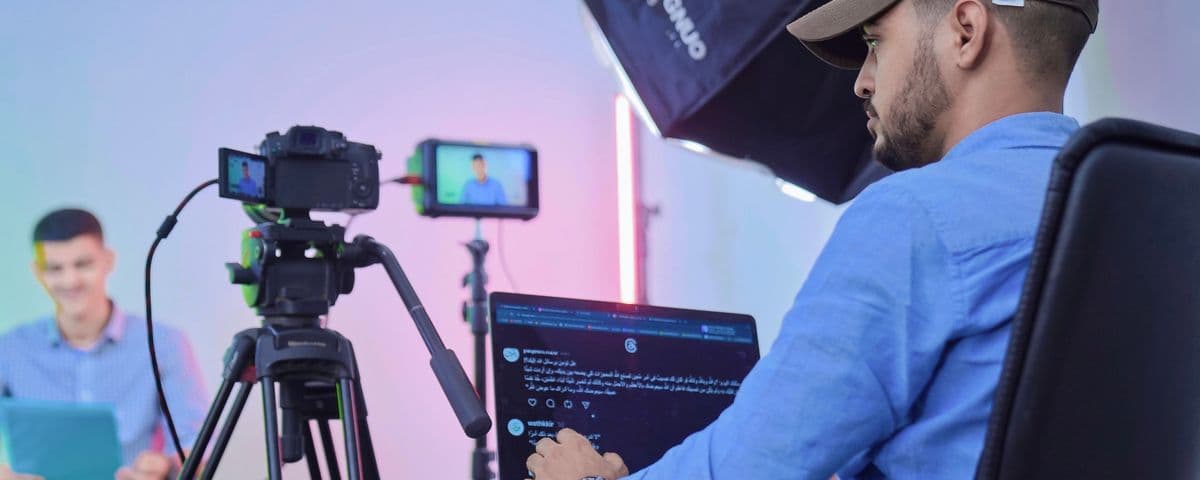 Bastidores de uma gravação: câmera no tripé, notebook e o apresentador ao fundo